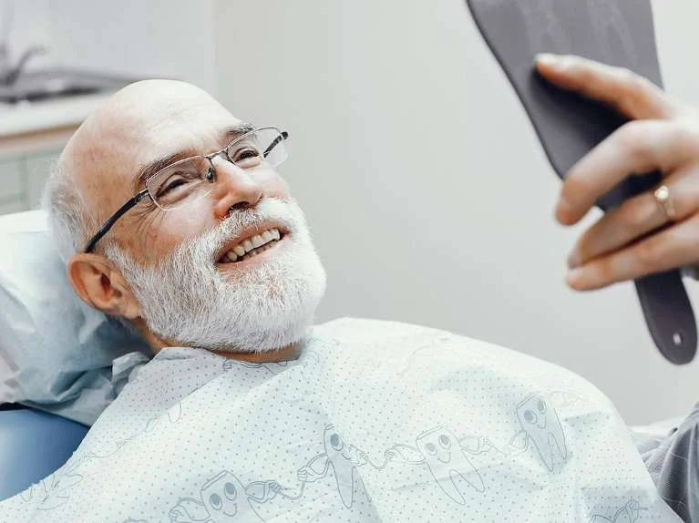 Smiling older man in the dental chair holding a mirror